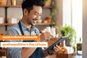 เจ้าของร้าน SME ยิ้มขณะดูภาพจากกล้องวงจรปิด LETcare บนแท็บเล็ต ภายในร้านค้าที่อบอุ่นและปลอดภัย